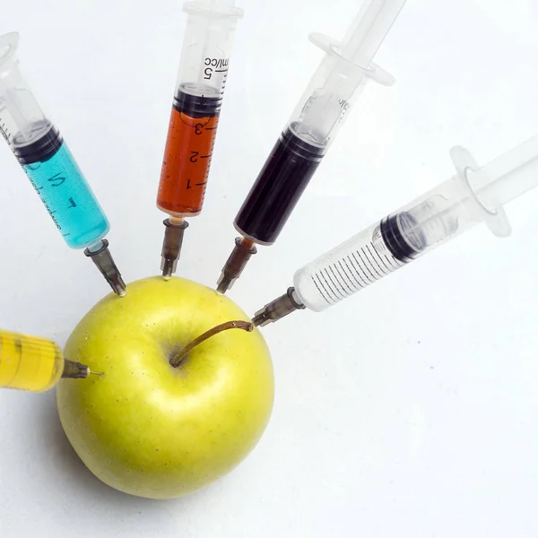 Nitrates, pesticides, fungicides and other chemicals are injected into a green apple with a syringe. Nearby is a magnifying glass. The concept of GMO and genetically modified organism. Close up. — Stock Photo, Image