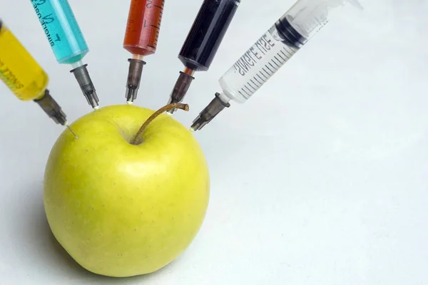 Nitratos, pesticidas, fungicidas y otras sustancias químicas se inyectan en una manzana verde con una jeringa. Frutas naturales y no transgénicas sin aditivos químicos . — Foto de Stock