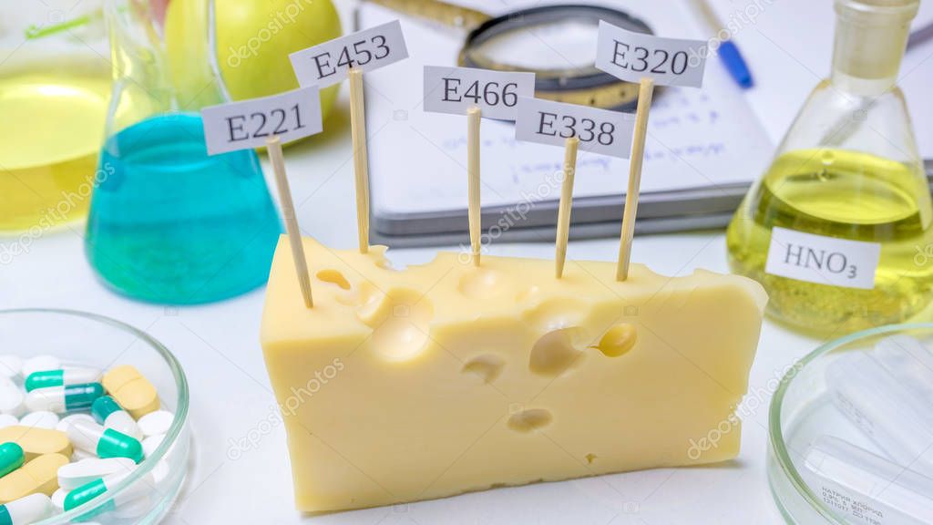 Harmful food additives. In the cheese are signs with the code E-supplements. Next On the table are flasks and a notebook with notes.