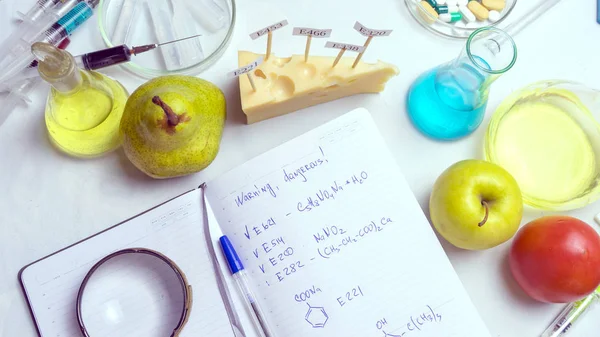 Procedimiento de laboratorio de seguridad alimentaria, analizando las frutas del mercado. Cuaderno y bolígrafo azul en la mesa del laboratorio. En el queso hay signos con el código E-suplementos. vista superior —  Fotos de Stock