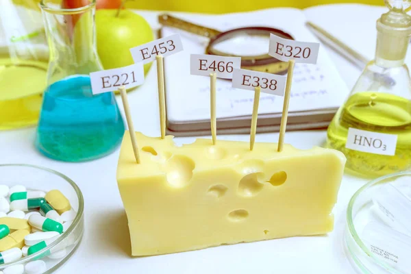 En el queso hay signos con el código E-suplementos. Cerca En la mesa hay un matraz de ácido nítrico, el principal nitrato. Aditivos alimentarios nocivos . — Foto de Stock