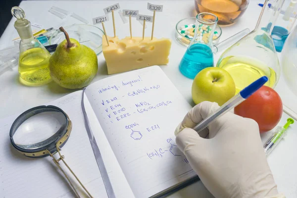 Gıda güvenliği müfettişi pazardan meyve test ediyor. Araştırma raporu ve laboratuvar masasında mavi kalem olan defter.