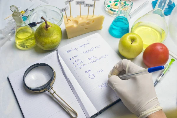 Gıda güvenliği müfettişi pazardan meyve test ediyor. Araştırma raporu ve laboratuvar masasında mavi kalem olan defter.