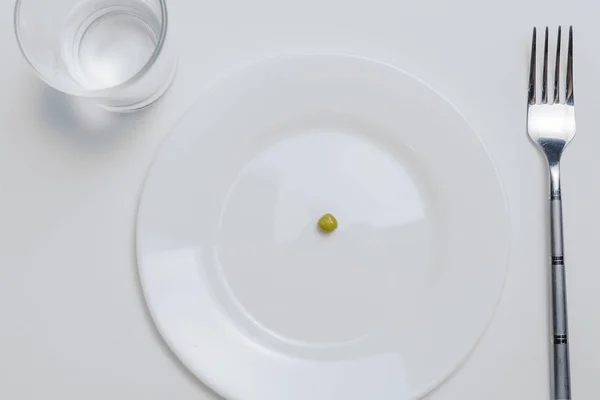 Concetto di dieta. un pisello su un piatto bianco vuoto con forchetta — Foto Stock
