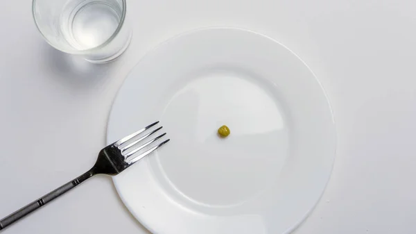 Concetto di dieta. un pisello su un piatto bianco vuoto con forchetta — Foto Stock