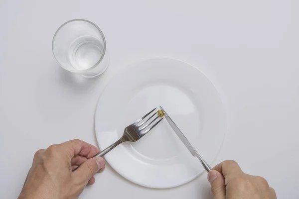 Thème Alimentation saine : mains tenant couteau et fourchette sur une assiette avec des petits pois verts sur une table blanche vue du dessus — Photo