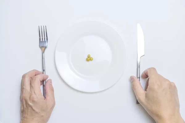 Tema de comida saludable: manos sosteniendo cuchillo y tenedor en un plato con guisantes verdes en una mesa blanca vista superior —  Fotos de Stock