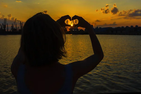 Woman making heart with hands in sunset. Love symbol in sunny summer night. Happy and carefree lifestyle.