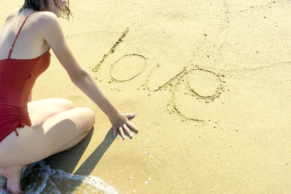 Das Mädchen schreibt das Wort Liebe in den Sand des Meeres, der Buchstabe o ist in Herzform gezeichnet. — Stockfoto