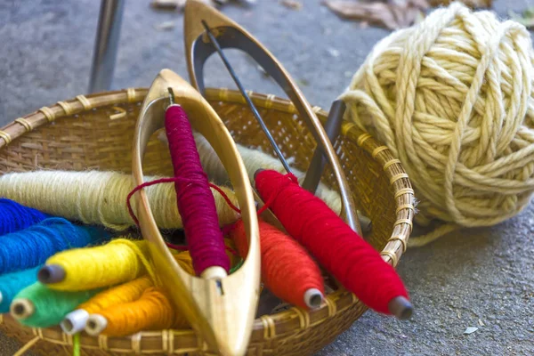 Tools for a loom in a basket: cotton yarn dyed in natural colors, shuttle, ball of thread. Close-up. — Stock Photo, Image