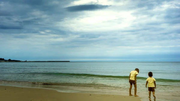 Zwei kleine Kinder Jungen am Strand des Ozeans. lustige niedliche Kinder, Geschwister und beste Freunde machen Urlaub und genießen den Sommer an stürmischen, windigen Tagen. — Stockfoto