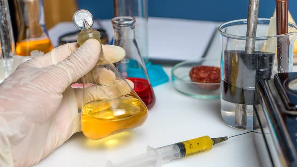 Photo Laboratory assistant hand holds flask, test tubes and laboratory equipment. Food laboratory. Close up on a white table.