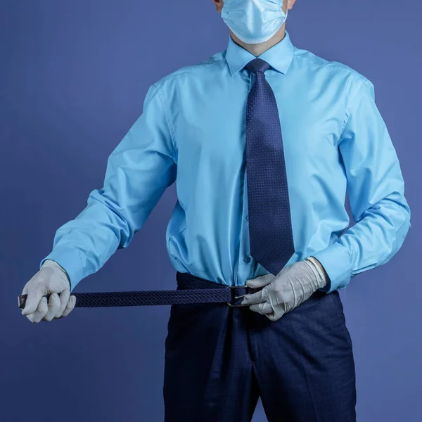 Photo Businessman in a medical mask and medical gloves tightens a belt on his pants, isolated on background. Business crisis during a pandemic.