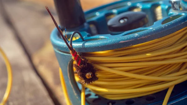 Fly Fishing Reel: İyi kullanılmış bir balık oltası, sinekle balık avlamak için yapılmış bir yemle birlikte deri kılıfının üzerinde oturur.. — Stok fotoğraf