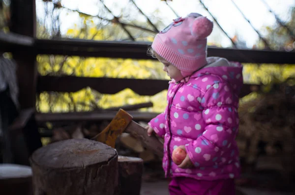 Тепло одетая маленькая девочка на фоне старого топора . — стоковое фото