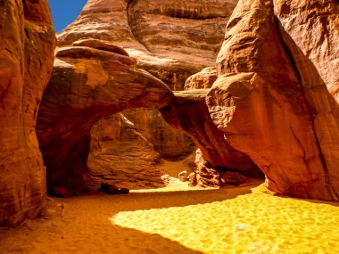 Mavi gökyüzünün altındaki kaya kemeri ve öğleden sonra güneşinde parlayan kum kemeri, Arches Ulusal Parkı, UT, ABD