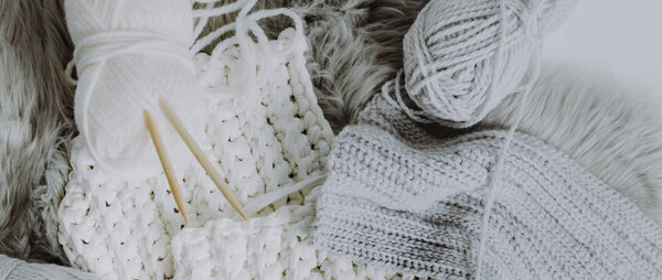 Уютная композиция из белой и серой шерсти с крючком и вязальными спицами
