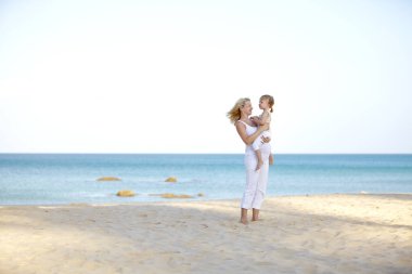 Genç hamile kadın holdings bebek kum plajındaki kollarında 