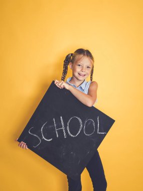 şirin kız öğrenci gülümseyen ve blackboard kelime okul ile tutarak ve turuncu arka plan önünde poz ise kameraya bakıyor 