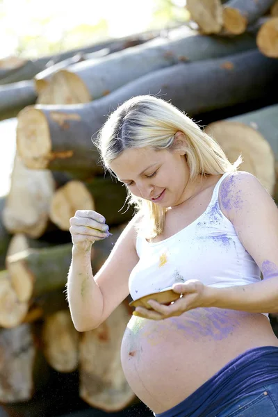 blonde pregnant woman pouring powder color on belly outside