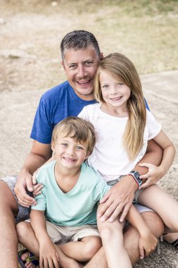 Mutlu ve çocuklu bir baba sahilde sarılıyor.