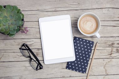 Ofis masası, tablet ve bir fincan kahveyle ahşap masada.