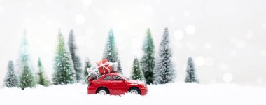 Minyatür kırmızı arabasıyla Karlı Kış Ormanı Noel ağacı ve hediyeler taşıyor.