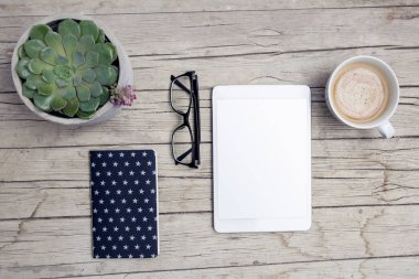 Ofis masası, tablet ve bir fincan kahveyle ahşap masada.