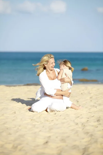 Giovane Donna Incinta Abbracciare Figlia Mentre Seduto Sulla Spiaggia Sabbia — Foto Stock