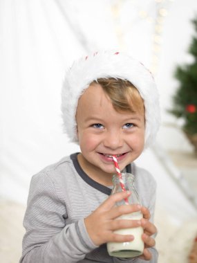 şişe tutan ve saman evde süt içmek kırmızı santa claus şapka giyen çocuk 