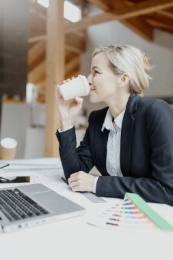 Şantiyede takım elbiseli çekici genç bir kadın mimar planla çalışırken kahve içiyor.