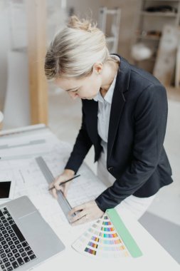 Şantiyedeki takım elbiseli çekici genç bayan mimar planlarla çalışıyor.