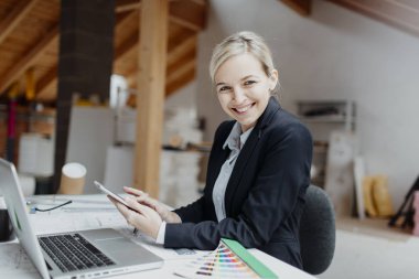 genç kadın mimar laptop ve planları ile çatı katında masada otururken Tablet PC'yi kullanma 