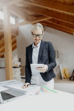 genç kadın mimar dizüstü bilgisayar ve planları loft adlı tablo yakın dururken Tablet PC'yi kullanma 