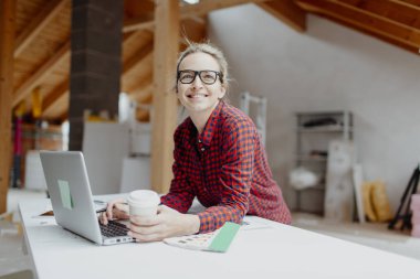 Bardaktan kahve içme ve çatı katında dizüstü bilgisayarda çalışan sarışın kadın