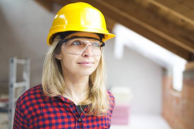 blonde woman with yellow helmet and green gloves planning expansion of loft