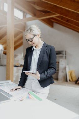 genç kadın mimar dizüstü bilgisayar ve planları loft adlı tablo yakın dururken Tablet PC'yi kullanma 