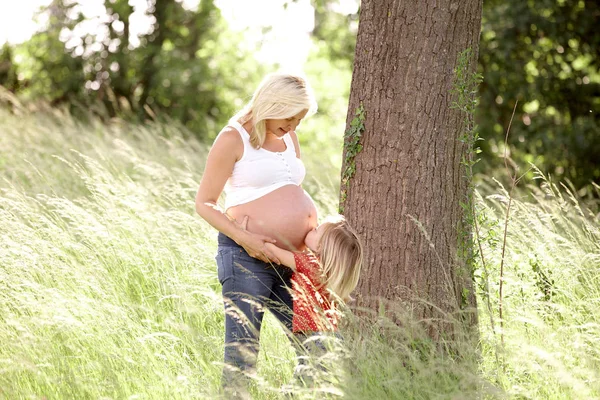 Córeczkę Obejmując Brzuch Ciąży Matki Pobliżu Drzewa Łące — Zdjęcie stockowe