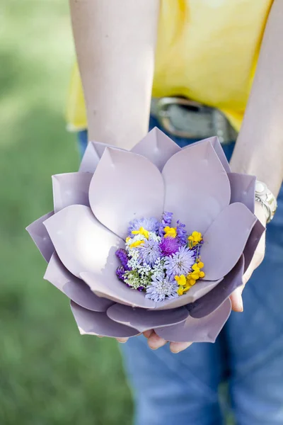 牧草地で花と美しい紫色の花のボウルを保持する女性の手 — ストック写真