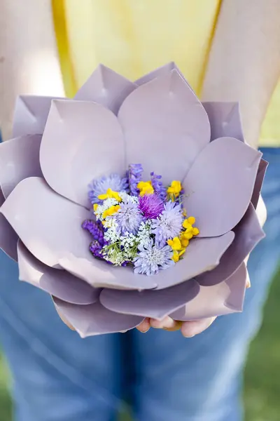 牧草地で花と美しい紫色の花のボウルを保持する女性の手 — ストック写真