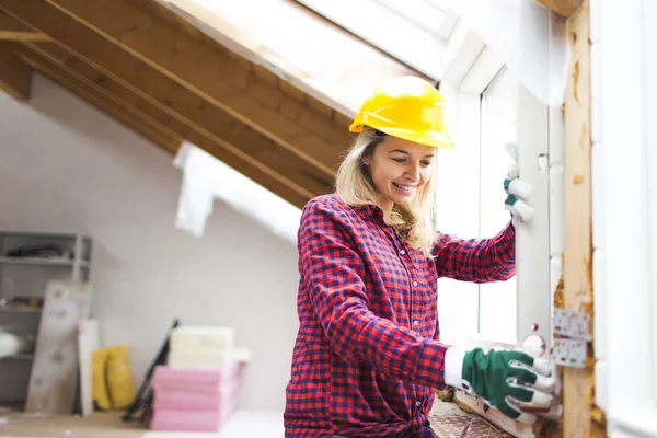blonde woman with yellow helmet and green gloves planning expansion of loft