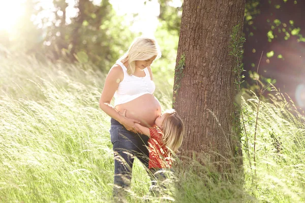 Fetiță Îmbrățișând Burta Mamei Însărcinate Lângă Copac Pajiște — Fotografie, imagine de stoc