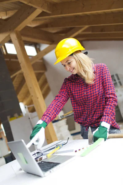 blonde woman with yellow helmet and green gloves planning on laptop expansion of loft