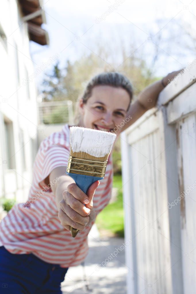 young beautiful woman painting in white color fence at summer 