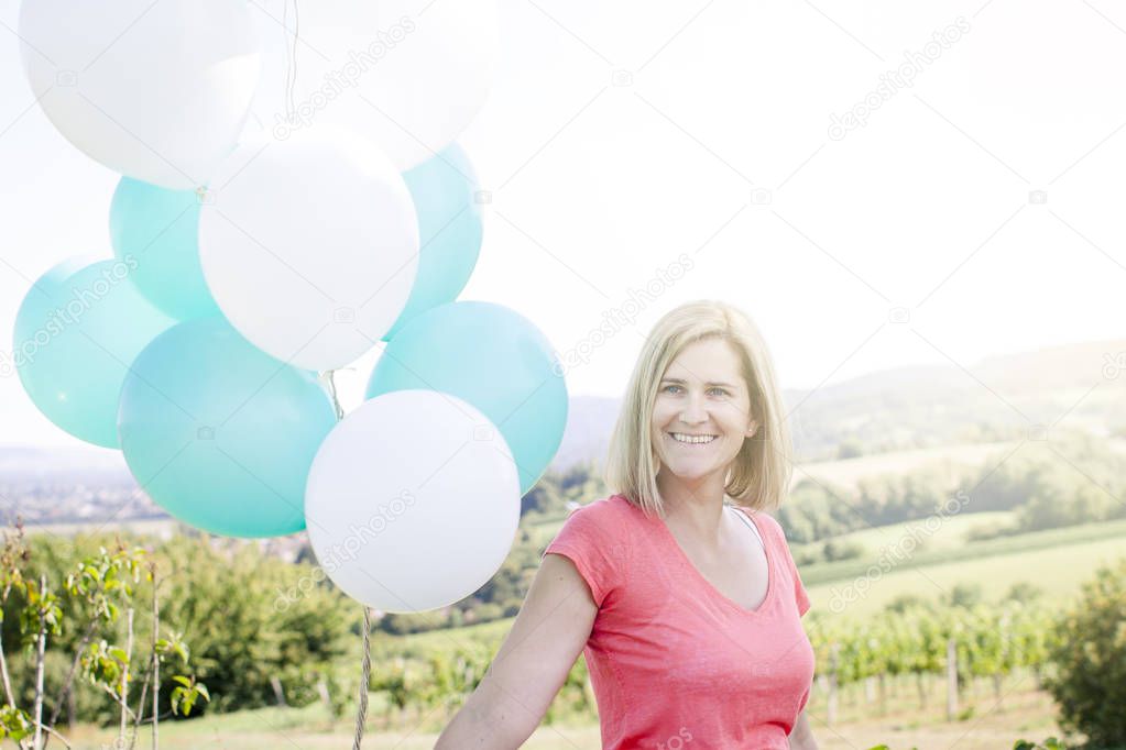 Happy woman with balloons having fun on meadow at summer sunny day 