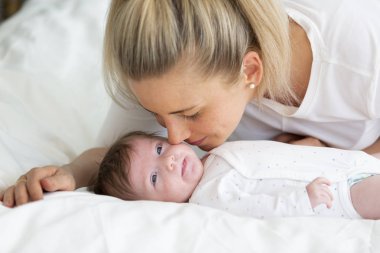 Beyaz gömlekli güzel sarışın kadın küçük kızıyla yatakta sarılıyor.