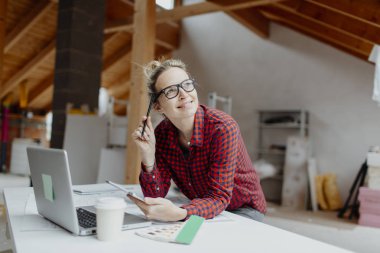 genç kadın mimar laptop ve planları ile çatı katında masada otururken Tablet PC'yi kullanma 