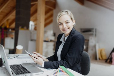 genç kadın mimar laptop ve planları ile çatı katında masada otururken Tablet PC'yi kullanma 