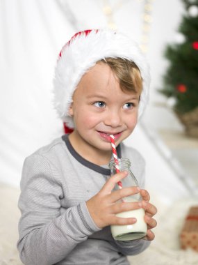 şişe tutan ve saman evde süt içmek kırmızı santa claus şapka giyen çocuk 