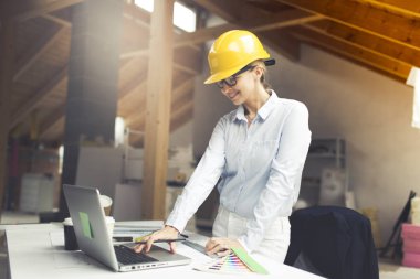 evde çatı dizüstü bilgisayar ile masanın yanında poz sarı kask ve beyaz gömlek giyen güzel genç kadın mimar